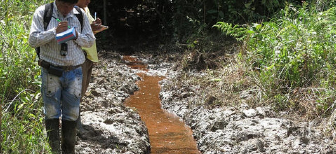 Two men observe and take notes on a polluted stream